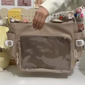 A plain khaki Ita messenger bag with an empty transparent front pocket, showing the DIY display area for anime pins and accessories