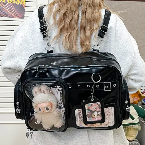 Black ita bag worn as backpack with clear window showing plush toy and badge